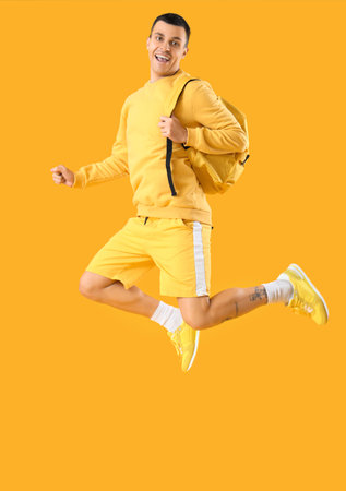 Male student with backpack jumping on yellow background