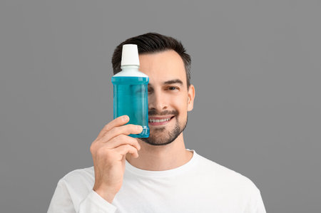 Handsome man with mouth rinse on gray background, closeupの写真素材