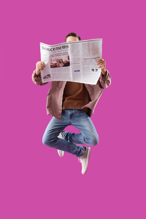 Young man with newspaper jumping on purple backgroundの写真素材