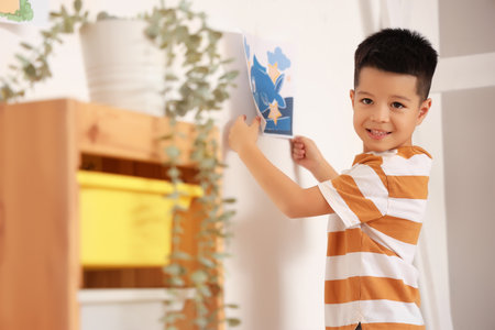 Little Asian boy hanging his drawing on wall at homeの写真素材