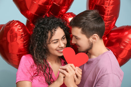Young couple with air balloons and paper heart for Valentine's day on blue backgroundの写真素材