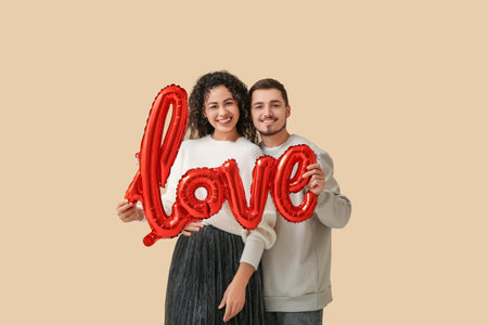 Young couple with air balloon in the shape of the word LOVE for Valentine's day on beige backgroundの写真素材