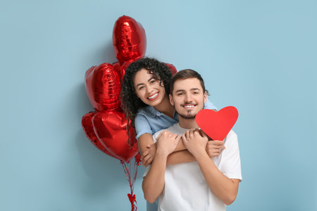 Young couple with paper heart and air balloons for Valentine's day on blue backgroundの写真素材