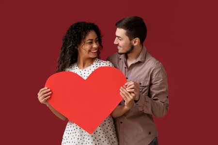 Young couple with paper heart for Valentine's day on red backgroundの写真素材