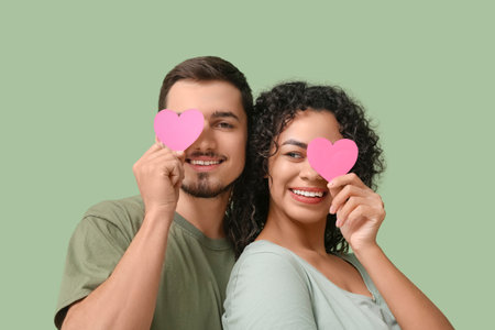 Funny young couple with paper hearts for Valentine's day on green backgroundの写真素材
