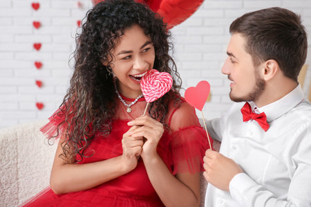 Young couple with heart-shaped lollipop for Valentine's day at homeの写真素材