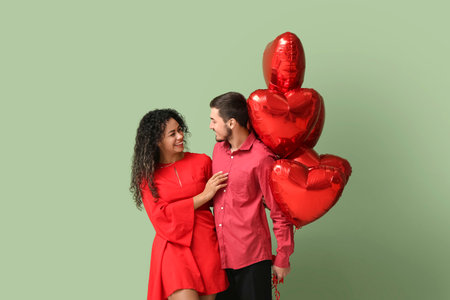 Young couple with air balloons in shape of heart for Valentine's day on green backgroundの写真素材