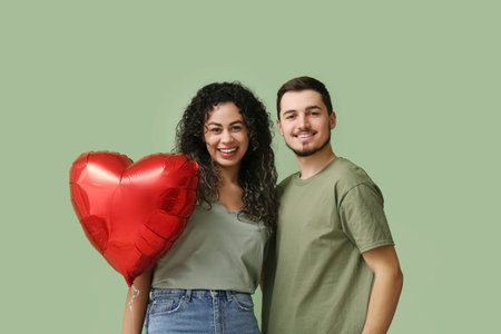 Young couple with air balloon in shape of heart for Valentine's day on green background