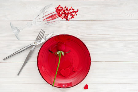 Beautiful table setting with red rose and confetti on white wooden background. Valentine's Day celebrationの写真素材