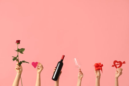 Female hands with hearts, red rose, gift box, glass and bottle of wine on pink background. Valentine's Day celebrationの写真素材