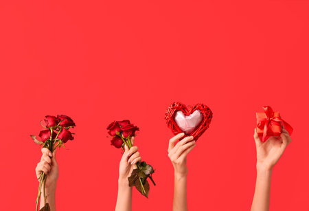 Female hands with heart, red roses and gift box on color background. Valentine's Day celebrationの写真素材