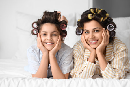 Little girl and her mother with hair curlers lying in bedroomの写真素材