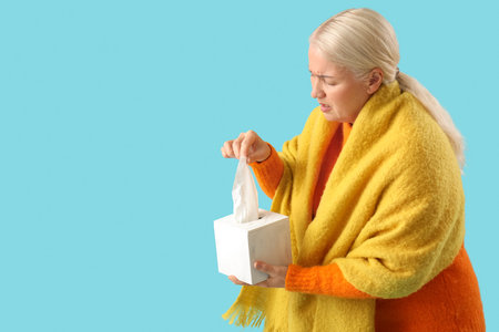 Sick mature woman taking tissue from box on blue backgroundの写真素材