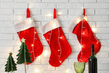Beautiful Christmas socks with glowing garland hanging on white brick wallの写真素材