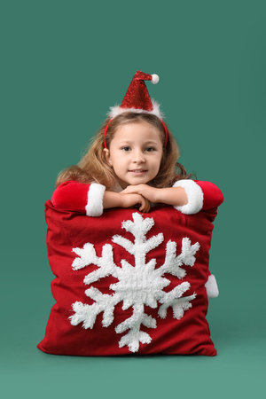 Cute little girl in Santa Claus costume with beautiful Christmas cushion on color backgroundの写真素材