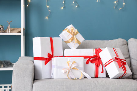 Different Christmas gifts on comfortable sofa against color wall