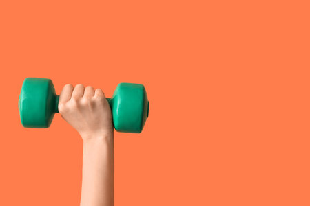 Female hands with dumbbell on orange backgroundの写真素材
