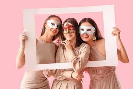 Beautiful young women in carnival masks with frame on pink backgroundの写真素材