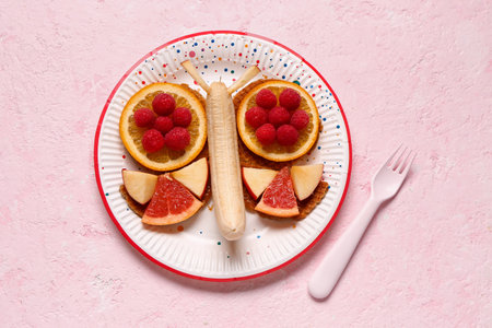 Plate with funny children's breakfast in shape of butterfly on pink tableの写真素材