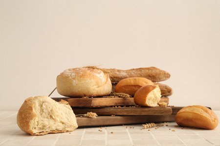 Boards with loaves of different fresh bread and wheat spikelets on white tiled tableの写真素材