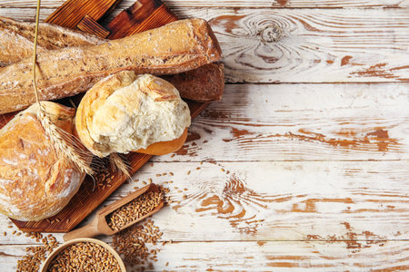 Loaves of fresh bread with wheat spikelets and grains on white wooden background