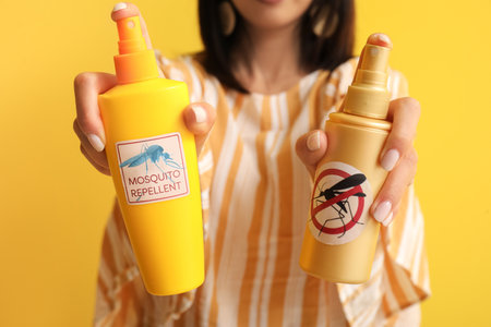 Young woman with mosquito repellents on yellow background, closeupの写真素材