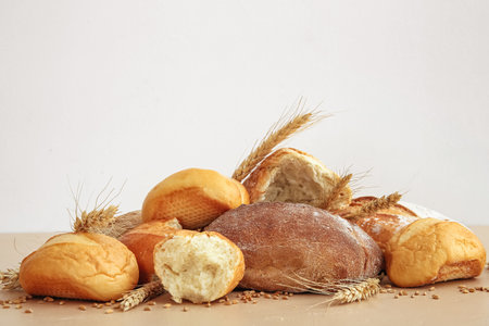Loaves of fresh bread and wheat spikelets on table against white backgroundの写真素材
