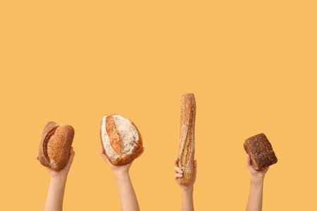 Female hands holding loaves of different fresh bread on orange backgroundの写真素材