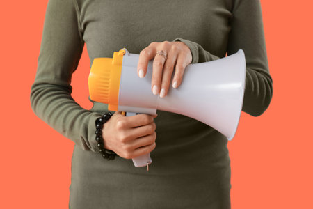 Young woman with megaphone on orange background, closeupの写真素材