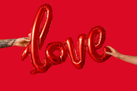 Man and woman with air balloon in the shape of the word LOVE on red background. Valentine's Day celebrationの写真素材