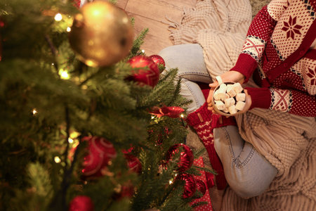 Woman with cup of hot chocolate sitting on floor near Christmas tree, closeupの写真素材