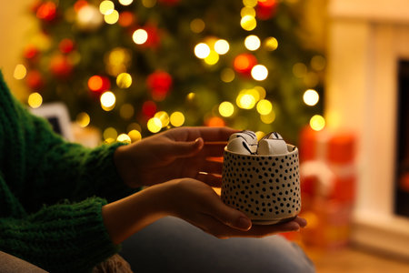 Woman holding cup of hot chocolate with marshmallows in festive living room, closeupの写真素材