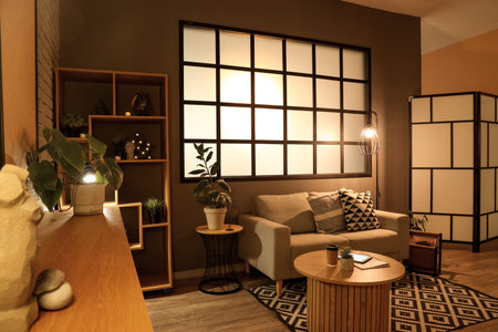 Interior of modern living room with gray sofa, coffee table, wooden cabinet and glowing lamps at eveningの写真素材