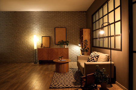 Interior of modern living room with gray sofa, coffee table and glowing lamps at eveningの写真素材