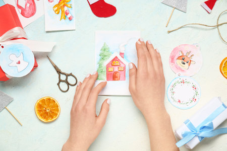 Female hands with beautiful Christmas card, gifts, scissors and decor on light background, closeupの写真素材