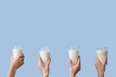 Hands with glasses of milk on light blue backgroundの写真素材