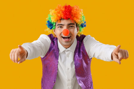 Happy young man in clown costume pointing at viewer on yellow backgroundの写真素材