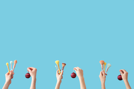 Hands holding makeup brushes and Christmas decorations on blue backgroundの写真素材