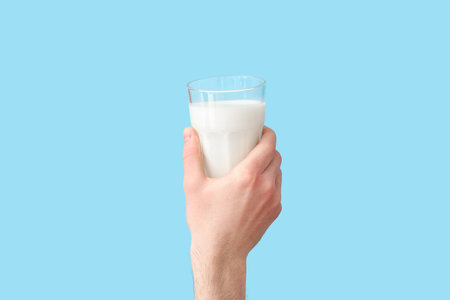 Hand with glass of milk on blue backgroundの写真素材