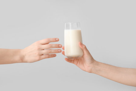 Hands handing over glass of milk on gray backgroundの写真素材