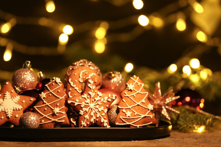 Plate with Christmas gingerbread cookies and balls on table against blurred lights