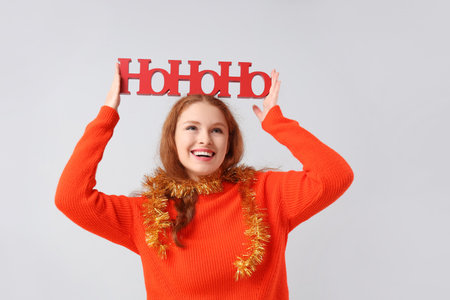 Young woman with Christmas greeting on light backgroundの写真素材