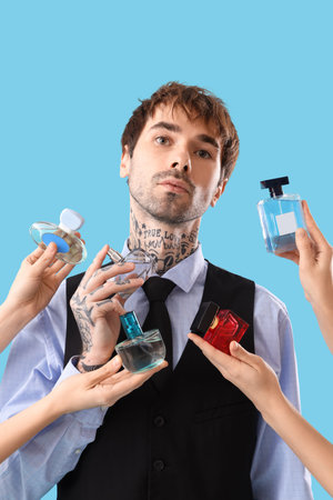 Tattooed young man and hands with bottles of perfume on blue background, closeupの写真素材