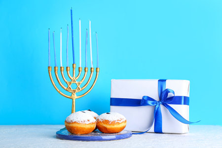 Plate with tasty donuts, menorah and gift for Hanukkah celebration on light tableの写真素材