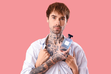 Tattooed young man with perfume and female hands on pink backgroundの写真素材