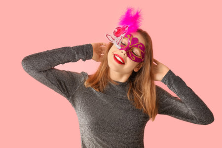 Beautiful young woman in carnival mask on pink backgroundの写真素材