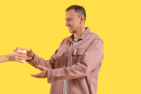 Mature man taking glass of milk on yellow backgroundの写真素材