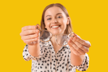 Young woman with eyeglasses on yellow background, closeupの写真素材