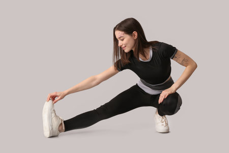 Sporty young woman stretching on light background