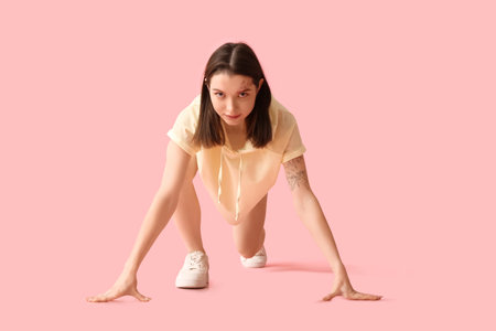 Sporty young woman getting ready to run on pink backgroundの写真素材